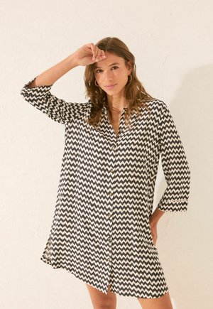 Kleid mit Knopfleiste, das ein Schwarz-Weiß-Zickzackmuster zeigt, lange Ärmel, einen Kragen und einen lässigen Schnitt mit Seitenschlitzen hat.