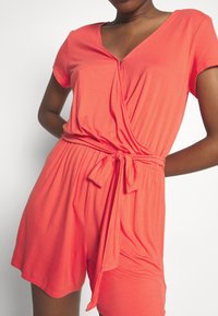 Mono corto de color coral con mangas cortas, escote en V, diseño cruzado y cinturón atado en la cintura. Fabricado con una tela suave y lisa que ofrece un ajuste relajado.