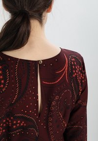 Abito bordeaux con stampa paisley, scollatura tonda, apertura a chiave sul retro chiusa da un bottone. Tessuto liscio con leggero lucido e texture.