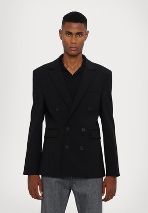 Black double-breasted blazer, structured design, wide lapels, three buttons, two front pockets, textured fabric, slightly oversized fit.