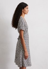 Schwarzes und weißes Kleid mit kurzen Ärmeln und Blumenmuster, V-Ausschnitt, taillierter Taille und weitem Rock, seitlich betrachtet.