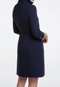 Marineblaues Kleid mit hohem Kragen, dreiviertel Ärmeln, figurbetontem Design und Schlitzen an den Ärmelsäumen. Glattes Material mit einer maßgeschneiderten Silhouette.