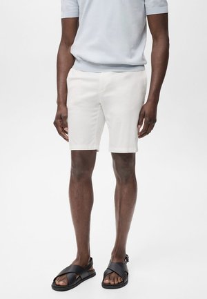 Shorts blancs en tissu léger, avec une coupe droite, des poches latérales et une finition soignée. Associés à des sandales à glissière noires.