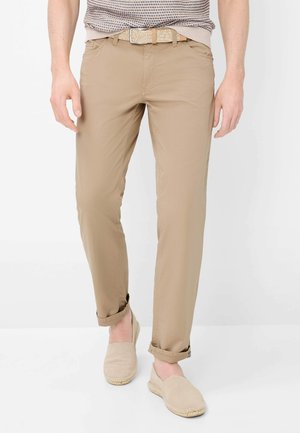 Uomo che indossa pantaloni chinos beige risvoltati, cintura intrecciata e scarpe espadrillas slip-on, con una maglia lavorata a maglia infilata dentro.