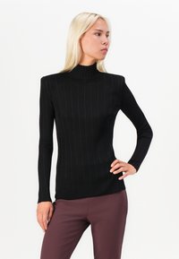 Top de malha preta, com gola alta, mangas longas, apresentando um design justo e uma textura macia. Combinado com calças justas cor vinho.