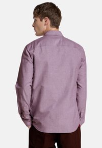 Camisa de manga larga morada con textura sutil, puños con botones y un cuello estructurado. La vista trasera muestra una silueta recta y detalles de costura.