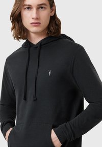 Felpa nera con tasca a marsupio, coulisse regolabile e logo a teschio discreto sul petto; realizzata in tessuto morbido e elasticizzato.