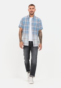 Blau-weißes kariertes Kurzarmhemd aus Baumwolle, mit Knopfleiste, kombiniert mit dunklen Jeans und weißen Sneakers.