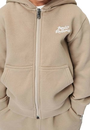 Beige hættetrøje med lynlås, frontlomme, ribstrikkede ærmeender og broderet logo på brystet. Blødt bomuldsmateriale, afslappet pasform.