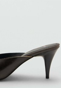 Mules de cuero negro de tacón alto con punta afilada, que presentan un diseño curvado, textura suave y tacón de aguja.