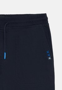 Navy blue shorts with an elastic waistband and drawstring. Features decorative blue and white stitching on the front pocket area.
