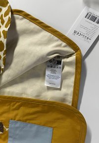 Interior de bolsa de algodón con tela beige, ribete amarillo y un bolsillo azul. Etiqueta de cuidado con símbolos y texto visibles. Hecho en Sri Lanka.