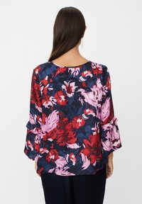 Blumenbluse mit dunklem Hintergrund und großen roten und rosa Blumen. Rüschensleeves sorgen für Textur. Glattes Material mit lockerer Passform.