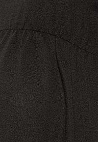 Tissu noir à surface texturée, présentant un léger plissage au niveau de la couture. Le matériau est léger avec une finition lisse.