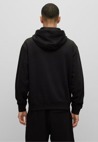 Sweat à capuche noir en mélange de coton, avec une coupe décontractée, des poignets côtelés et une poche kangourou. Texture lisse, design minimaliste.