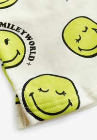 Biała tkanina z powtarzającymi się wzorami żółtych buziek. Posiada czarne kontury z napisem "SMILEYWORLD" nad jedną z buziek. Miękka tekstura.