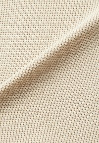 Tissu textile tricoté façon gaufre couleur crème, plié en diagonale, montrant un motif quadrillé texturé avec de petits carrés en relief.