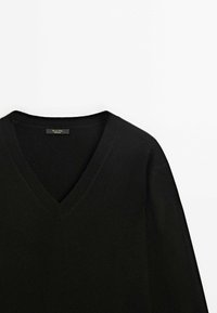 Pull noir à col V en matériau doux et tricoté fin. Doté de longues manches et d'un design épuré et simple avec une texture côtes subtile au niveau de l'encolure.