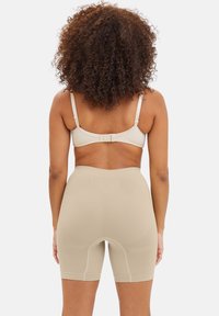 Pantalones cortos modeladores beige sin costuras con un corte a media muslo, textura suave y tirantes ajustables. Diseñados para ofrecer comodidad y uso discreto.