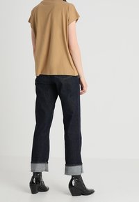 Top corto beige de mangas cortas combinado con jeans azul oscuro, doblados en el dobladillo, y botas de tobillo negras con tacón, con acentos brillantes.