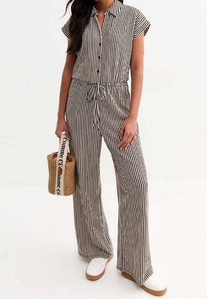 Combinaison rayée à manches courtes, boutonnée sur le devant, taille cintrée, jambes larges, motif noir et blanc, assortie à un sac tressé et des baskets.