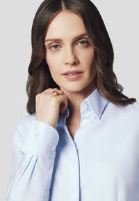 Jasnoniebieska koszula z długim rękawem wykonana z tkaniny wyróżniająca się mankietami z detalami w postaci guzików oraz subtelnym zagięciem w okolicy nadgarstka.