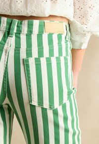 Rifle z denimu so zeleno-bielymi pruhmi, vybavené zadným vreckom a koženou značkovou štítkou. Pruhy sa striedajú v sýtych farbách.