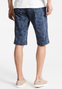 Blå shorts med ett ormbunksmönster, i bomullsliknande material, knälång, har fickor och en avslappnad passform. Bärs med ljusbruna slip-on skor.