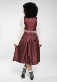Robe en satin bordeaux avec une jupe plissée, blouse blanche à manches longues et un accent en ruban rose à la taille. L'arrière possède une fermeture à boutons.
