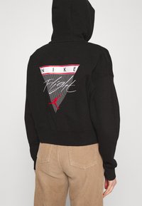 Sudadera con capucha negra con un gráfico triangular que presenta el texto "NIKE" y un logo de Jumpman rojo, fabricada en suave material de algodón.