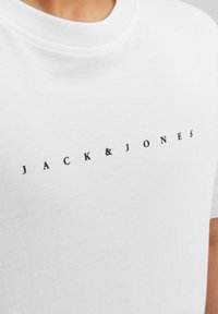 Balta medvilninė marškinėliai su apvalia iškirpte ir juodu „JACK & JONES“ logotipu, atspausdintu ant krūtinės. Mankšta tekstūra, laisvas siluetas.