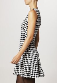 Mekko, jossa on mustavalkoinen houndstooth-kuvio, olkaimeton, tiukka vartalo, levenevä hame, sileä kangas, reiden puoliväliin saakka ulottuva pituus.