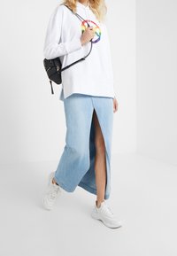 Sudadera blanca con un diseño de círculo de arcoíris, combinada con una falda de mezclilla azul claro con una abertura frontal y zapatillas blancas. Mochila negra.