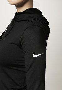 Sudadera deportiva negra hecha de tejido suave, con un bolsillo frontal, cordón ajustable y el logo blanco de Nike en la manga izquierda.