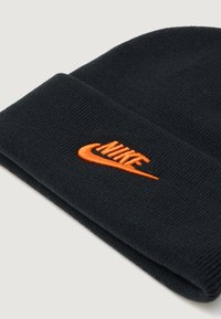 Črna pletena kapa s prepognjenim robom, ki ima na strani izvezen oranžen logotip Nike. Mehka tekstura in tesno prilega.