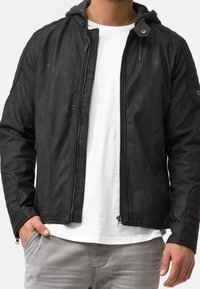 Musta nahkainen pommittajatakki, jossa on harmaa huppu, vetoketjukiinnitys, teksturoitu olkatyöstö ja sivutaskut.