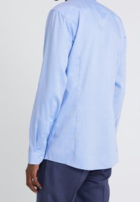 Světlomodrá košile s dlouhým rukávem z hladké látky, s úzkým střihem, manžetami na knoflíky a švem na zádech. Bez vzorů nebo dekorací.