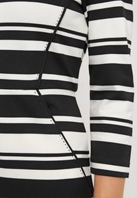 Gros plan d'un vêtement à manches longues rayé horizontalement noir et blanc avec un détail de couture diagonale sur le torse.