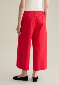 Rode, lichtgewicht, wijde broek met een elastische taille. Heeft een cropped lengte en een gladde textuur, gedragen met zwarte platte schoenen.