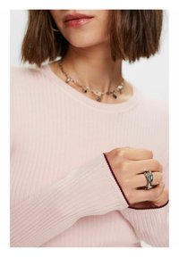 Haut à manches longues rose clair côtelé avec des poignets de couleur marron. Complété par un collier en argent à couches multiples et une bague argentée torsadée à la main.