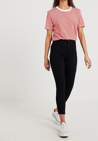 Červeno-bílý pruhovaný tričko s kulatým výstřihem, spárované s černými skinny džíny a bílými teniskami. Ležérní, přiléhavý střih po celé ploše.