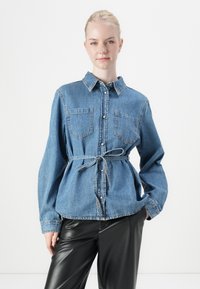 Denim shirt met lange mouwen, kraag, twee borstzakken, aansluitende taille met een strik en knoopsluiting in een lichtblauwe kleur.