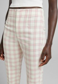 Plaid trousers in light cream with pink and black lines, featuring a fitted shape, smooth texture, and subtle crease down the front.