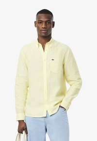 Camicia a righe gialle e bianche con bottoni, dotata di taschino, realizzata in un tessuto leggero e con un piccolo logo sul petto.