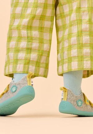 Kind trägt hellblaue Socken, grün-weiß karierten Hosen und graue Turnschuhe mit türkisfarbenen Sohlen und gelben Akzenten.