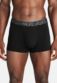 Črne bokserice z enotnim pasom, ki nosi bel napis "UNDER ARMOUR". Narejene so iz gladkega materiala in nudijo prilegan obliko s prednjim žepkom.
