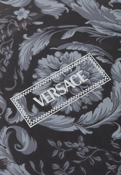 Juodas audinys su sudėtingu pilku gėlių raštu, su baltu "VERSACE" logotipu aptvertame stačiakampyje. Lygi tekstūra, elegantiškas dizainas.