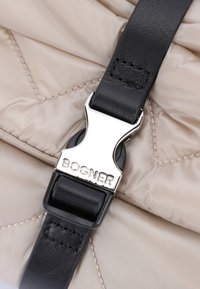Czarny skórzany pasek z srebrną metalową klamrą, oznakowany "BOGNER", przymocowany do strukturalnej beżowej pikowanej tkaniny. Czysty i minimalistyczny design.