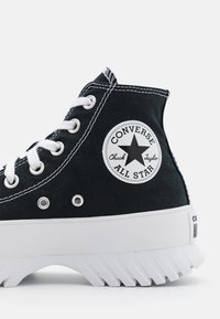 Sneaker alte in tela nera con lacci bianchi e suola in gomma. Presenta una toppa rotonda con logo e cuciture bianche a contrasto lungo le cuciture.