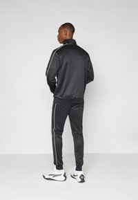 Black athletic tracksuit made of smooth fabric, featuring white side stripes, a standing collar, and fitted cuffs on both jacket and pants.